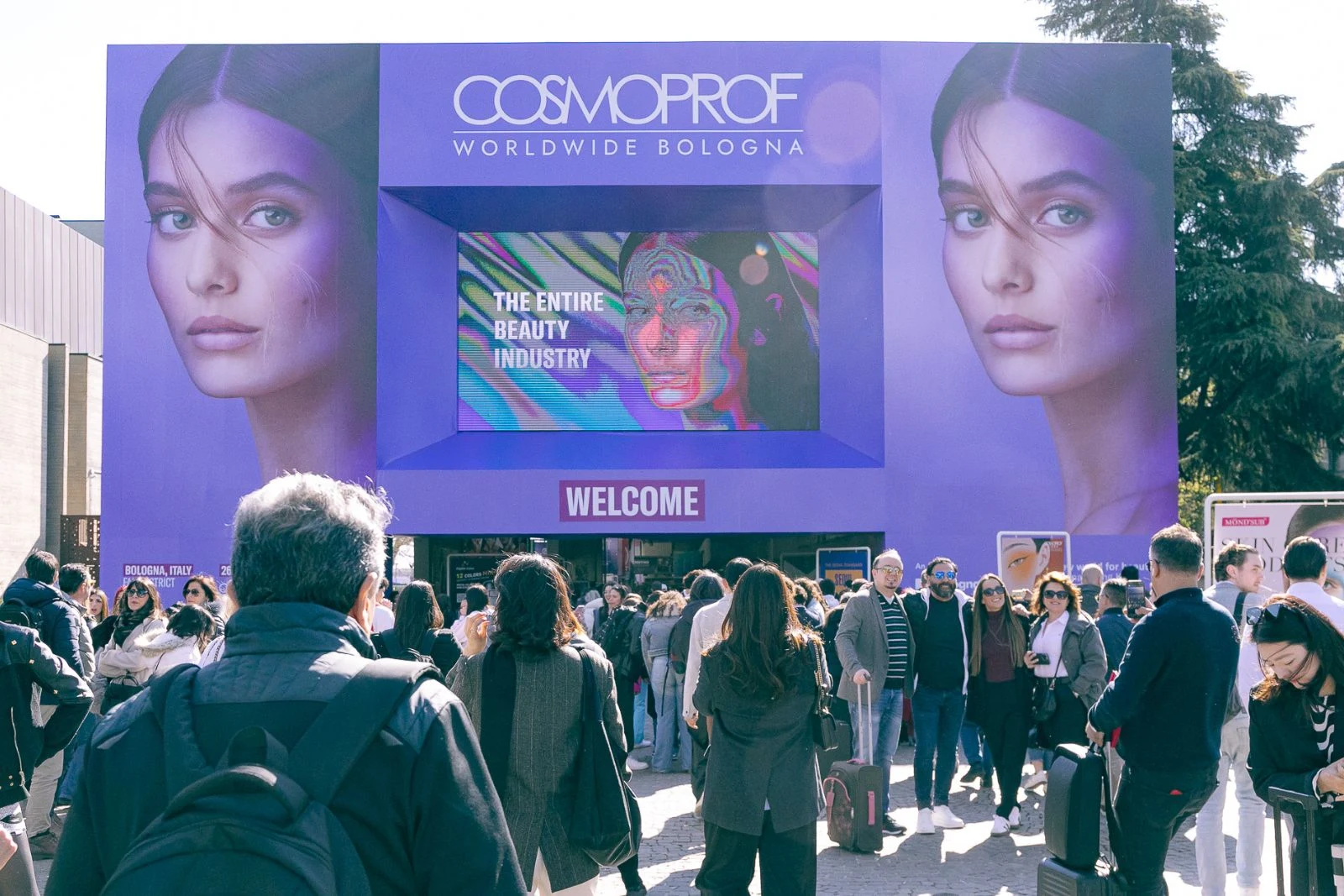 Visitors entering Cosmoprof Worldwide Bologna beneath the exhibition’s large welcome screens.
