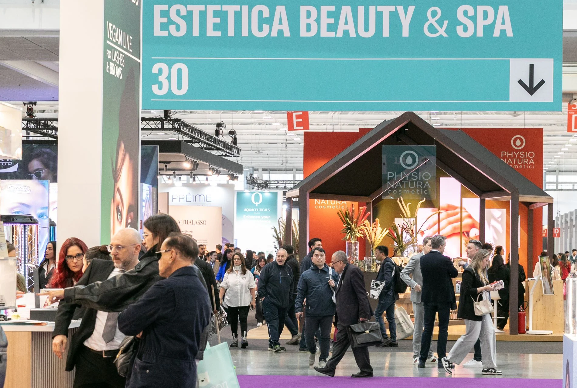 Visitors moving through a broad Cosmoprof show floor lined with constructed exhibition stands.