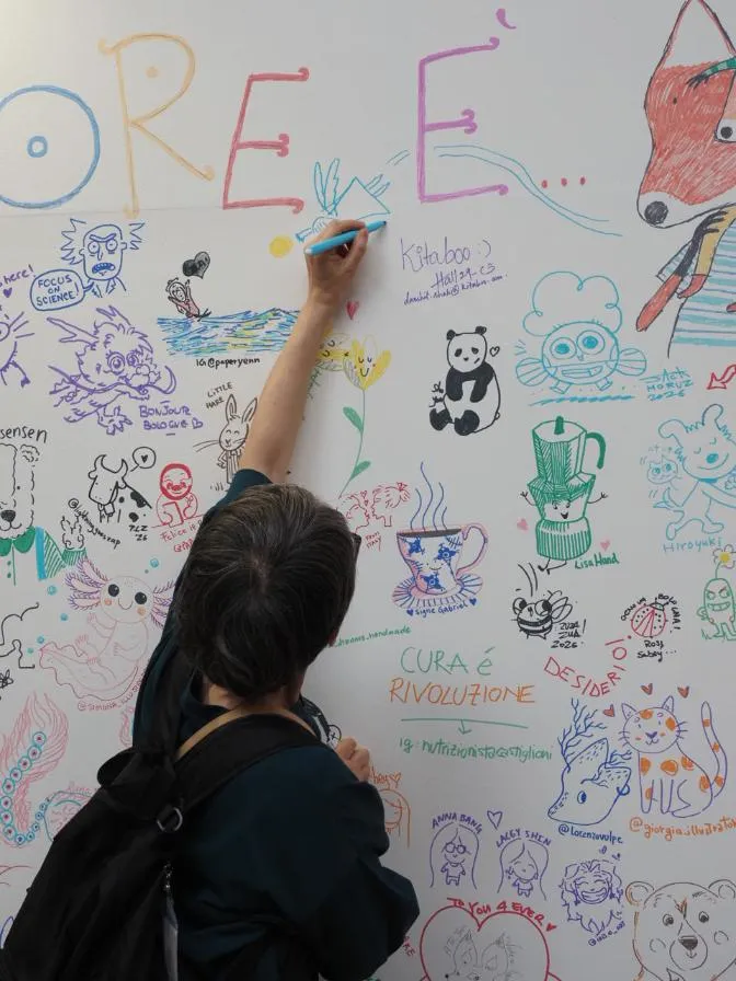 An illustrator adds a drawing to the crowded Illustrators Wall at BCBF 2026.